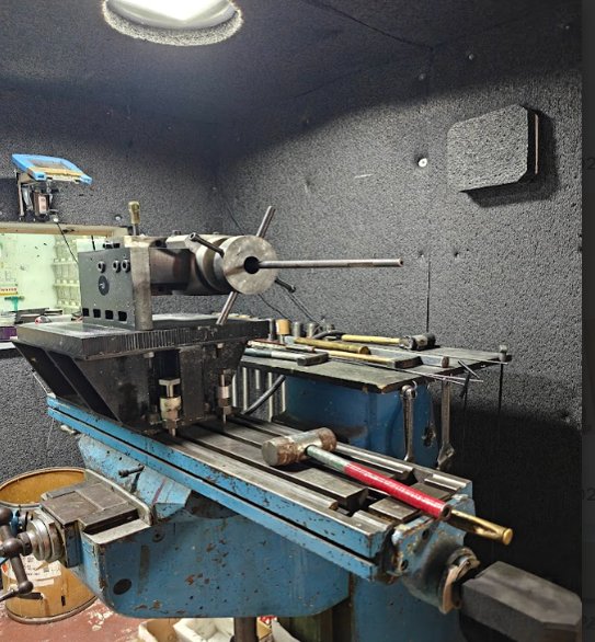 A live-fire ballistics test rig aimed at a mounted material sample inside a padded test chamber